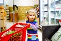 Cute todler girl pushing shopping cart in supermarket. Little child buying fruits. Kid grocery shopping. Adorable baby Royalty Free Stock Photo