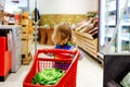 Cute todler girl pushing shopping cart in supermarket. Little child buying fruits. Kid grocery shopping. Adorable baby