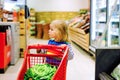 Cute todler girl pushing shopping cart in supermarket. Little child buying fruits. Kid grocery shopping. Adorable baby