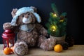 Cute toy bear holding a paw on a red lantern on a black background. In the frame, you can see a small Christmas tree with Royalty Free Stock Photo