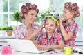 Cute twin girls and mother with hair curlers sitting at table