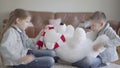 Portrait twin boy and girl sitting on the floor in living room and dont know how to share between them a big taddy bear