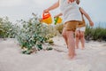 Cute unrecognizable little boys watering plants with cans on sandy beach. summer sunny day. Toddlers twins with colorful Royalty Free Stock Photo