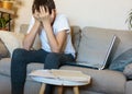 Cute upset boy in white t shirt sitting on the couch in the living room next to laptop and study. Stressed. tired kid. Royalty Free Stock Photo