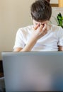 Cute upset boy in white t shirt sitting on the couch in the living room next to laptop and study. Stressed, tired kid. Home Royalty Free Stock Photo