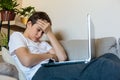 Cute upset boy in white t shirt sitting on the couch in the living room next to laptop and study. Stressed, tired kid. Home Royalty Free Stock Photo