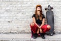 Cute urban girl with longboard sitting sitting next to a brick wall