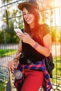 Cute urban girl in skatepark with skateboard using smart phone