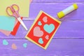 Cute Valentines day card made from colored paper. Scissirs, glue stick, colored paper sheets on a wooden table