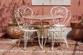 Cute vintage retro metal frame outdoor table and white chairs in front of house wall with large ceramic flower pots on stone tiles Royalty Free Stock Photo