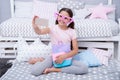 Cute vlogger streaming video. Girl child sit on bed in her bedroom and taking selfie or streaming video. Kid prepare to Royalty Free Stock Photo