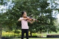 A cute white Asian girl is playing the violin in the middle of beautiful nature, greenery and sunlight Royalty Free Stock Photo