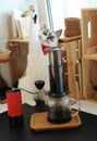 Cute white blue-eyed cat barista in a red bow tie brewing aeropress coffee. Alternative manual methods concept