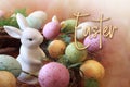 Cute white bunny in wreath of speckled eggs with the word Easter