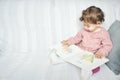 A cute white Caucasian girl sat on a sofa reading a children`s picture book Royalty Free Stock Photo