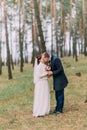 Cute white dressed bride with her handsome groom kissing in green pine forest