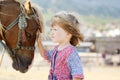 Cute white toddler girl in a rustic style dress caressing brown pony in a field in sunny day Royalty Free Stock Photo