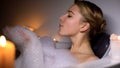 Cute woman in bath blowing bubbles, having fun, evening relaxation with candles