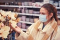 Cute woman in face mask chooses artificial flowers in shop Royalty Free Stock Photo