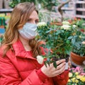 Cute woman gardener in face mask chooses white rose flowers in store Royalty Free Stock Photo