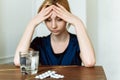 Cute woman holding her head and looking at a glass of water and pills. To feel bad. Coronavirus disease, covid-19. Feel sick Royalty Free Stock Photo