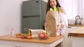 Cute woman holding paper bag put fruits and vegetables walk into the kitchen, place on table and wash her hands with gel alchol to