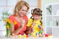 Cute woman and kid girl decorating Easter eggs at home