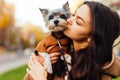 Cute woman kissing a cute little dog, close up portrait. Lady hugs a biewer terrier dog on the street. Love of woman owner and pet