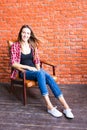 Cute woman with long legs sitting in the armchair behind a brick wall