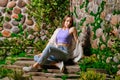 Cute woman sits on stone path surrounded with old overgrown stone wall in the park Royalty Free Stock Photo