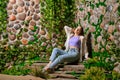 Cute woman sits on stone plate steps with old overgrown stone wall in the park Royalty Free Stock Photo