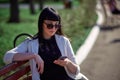 Cute Woman with Sunglasses and Long Hair is Using Mobile Device Enjoying Sunbeams and Warm Day Outdoors. Portrait of Smiling Royalty Free Stock Photo