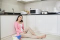 Cute woman using mobile phone sitting on a cleaned floor in kitchen