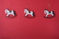 Cute wooden Christmas toys of white rocking horses on golden pendants on a festive red Christmas background. Royalty Free Stock Photo