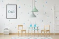 Cute, wooden furniture for children and a mock-up poster on a white wall with blue and green droplets in a modern kid playroom in Royalty Free Stock Photo