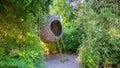 Cute wooden hut for relaxing. Woven with twigs and sticks. Hanging from a tree, ladder leaning against it.