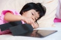 Cute 4 year old Asian girl is lying on the bed playing games with her tablet. Kid using the screen with touch screen. Royalty Free Stock Photo