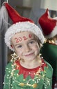 cute 6 year old boy in elf costume, santa hat, garland beads, New Year 2024 numbers written on forehead