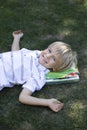 cute 6 year old boy lies on the grass with his head on the books looking up Royalty Free Stock Photo