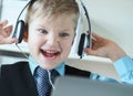 Cute 6 year old boy in suit listening to music or audio tutorial on headphones at the office background. Royalty Free Stock Photo