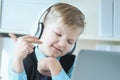 Cute 6 year old boy in suit listening to music or audio tutorial on headphones at the office background. Royalty Free Stock Photo