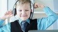 Cute 6 year old boy in suit listening to music or audio tutorial on headphones at the office background. Royalty Free Stock Photo