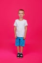 Cute 5-year-old boy in a white T-shirt and blue full-length shorts on a pink isolated background. Vertical Royalty Free Stock Photo