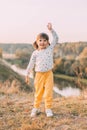 A cute 3-year-old girl with two ponytails and a polka-dot sweater stands on the river bank on a warm autumn day, Royalty Free Stock Photo