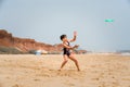 Cute youg girl in swimsuit standing on a beach by the sea throwing a green disc. Royalty Free Stock Photo