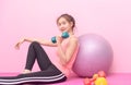 Cute younf girl lifting dumbbell on pink background