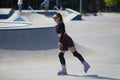 Cute young adult female riding on aggressive inline skates in a concrete skatepark. Roller blader chick in plaid skirt skating in