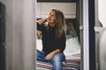 Cute young adult woman relax sitting in the bedroom inside a modern motor home camper van. Van life and traveler nomadic lifestyle