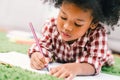 Cute young African American kid girl drawing or painting with colored pencil