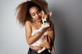 Cute young american african woman with curly hair hugging and kissing her puppy basenji dog. Love between dog and owner Royalty Free Stock Photo